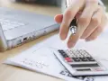 Pracownik wykorzystał cały urlop i się zwolnił. Dłoń z długopisem nad kalkulatorem i laptopem.