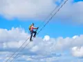 Frau klettert auf dem Donnerkogel Klettersteig über eine Hängebrücke, umgeben von blauem Himmel und Wolken.