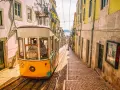 Żółty tramwaj zjeżdża po stromych uliczkach Lizbony. To klasyczny widok, który warto zobaczyć w Lizbonie, z kolorowymi budynkami i brukowanymi schodami.