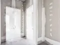Wnętrze w stanie deweloperskim. Widoczne nieotynkowane ściany, otwory drzwiowe i betonowa podłoga.