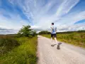 Uomo corre su strada sterrata, ideale per la preparazione 10 km principianti. Cielo azzurro con nuvole bianche.