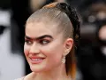 Primer plano de una mujer con una uniceja prominente, cabello recogido en coleta y pendientes llamativos.