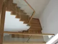 Nowoczesne schody dywanowe na beton, z drewnianymi stopniami i szklaną balustradą, tworzą lekkość i elegancję.