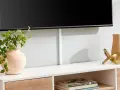 Snyggt sätt att bygga in tv:n med dold kabelhantering. En vas med gröna blad och en dekorativ guldfigur pryder möbeln.