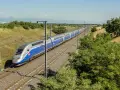 Niebiesko-srebrny pociąg dużych prędkości TGV na torach kolejowych, otoczony zielenią i słupami trakcyjnymi.