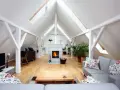 Aménagement comble 30m2 : salon cosy avec cheminée, canapé gris, parquet clair et poutres apparentes.