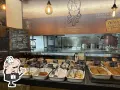A display case filled with small dishes of food, with a chalkboard menu and a restaurant logo in the background.
