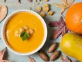 Un reconfortante tazón de puré de calabaza, adornado con picatostes y perejil, junto a calabazas, hojas de otoño y nueces.