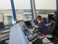 Kontroler ruchu lotniczego, mimo młodego wieku, skupiony na monitorach. Widok na lotnisko i samoloty.
