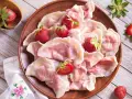 Pyszne pierogi z truskawkami, ozdobione świeżymi owocami, wyglądają apetycznie na glinianym talerzu.