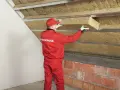 Pracownik w czerwonym kombinezonie Rockwool montuje izolację na ścianie szczytowej poddasza.