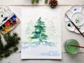 Pintura de acuarela de un árbol de Navidad nevado, con una paleta de acuarelas y pinceles, ideal para una acuarela navidad facil.