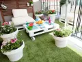 Balcón acogedor con césped artificial, muebles de palets y macetas con flores. ¡Ideas para terrazas con césped artificial!
