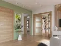 Un pasillo con paredes verde menta y puertas de roble. Un cuadro de hojas tropicales y un jarrón con flores adornan la pared.