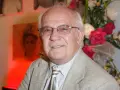 Uśmiechnięty Jerzy Antczak, reżyser znany z niezapomnianych filmów, w eleganckim garniturze, na tle bukietu kwiatów i portretu.