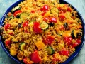 Un piatto colorato di cous cous con verdure miste: peperoni rossi e gialli, zucchine e melanzane.