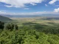 Rozległy widok na krater Ngorongoro z bujną zielenią na pierwszym planie i jeziorem w oddali.