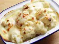 Coliflor gratinada con bechamel cremosa, dorada y burbujeante en una fuente.