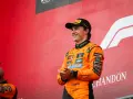 El piloto australiano F1, Oscar Piastri, sonríe en el podio con su mono naranja de McLaren.