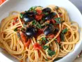 Un piatto invitante di spaghetti alla puttanesca, con olive nere, capperi e pomodoro fresco, guarnito con prezzemolo.