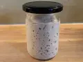 Ein Glas mit Sauerteig, dessen Konsistenz durch viele kleine Bläschen und eine luftige Struktur gekennzeichnet ist.