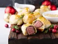 Bouchées à la reine dorées, garnies de viande juteuse, sur une planche en bois avec des canneberges et des décorations festives.