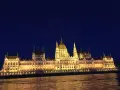 Budynek Parlamentu w Budapeszcie nocą, oświetlony, z odbiciem w Dunaju. Warto sprawdzić ceny na Węgrzech przed podróżą.
