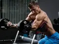 Mężczyzna wykonuje ćwiczenia na biceps i triceps z użyciem sztangi łamanej na modlitewniku.