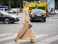 Elegancka kobieta w beżowej sukience i złotych sandałach przechodzi przez pasy.