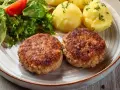 Dwa apetyczne kotlety mielone z airfryer, podane z ziemniakami i świeżą sałatką.