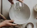 Wasser wird in eine Schüssel gegossen, vielleicht zu viel Wasser im Brotteig. Ein Nudelholz liegt daneben.