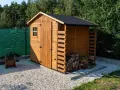 Drewniany domek na narzędzia ogrodowe, z małym okienkiem i drzwiami, obok stos drewna.