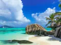Rajska plaża na Seszelach. Turkusowa woda, biały piasek, palmy i charakterystyczne granitowe skały tworzą idylliczny krajobraz. Na horyzoncie żaglówka.