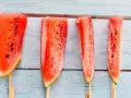 Vier gefrorene Wassermelonenstücke auf Stöcken, bereit zum Genießen. Eine erfrischende Idee für Wassermelone einfrieren.