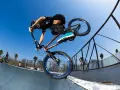 A BMX rider, possibly Chelsea Wolfe, performs a trick on a ramp against a clear blue sky.