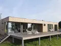 Nowoczesne domy modułowe pod klucz z drewnianą elewacją i dużymi przeszkleniami, stojące na tarasie z widokiem na zieleń.
