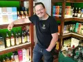 Mann in einem Guinness-T-Shirt steht in einem Laden voller Whisky-Flaschen und -Schachteln. Er lächelt und lehnt sich an ein Regal.