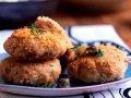 Polpette tonno e patate dorate e croccanti, guarnite con erbe aromatiche e olive, pronte per essere gustate.