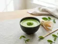 Zielona, spieniona matcha w miseczce, obok bambusowa miotełka i łyżeczka. Idealna na chwilę relaksu. Gdzie kupić taką matchę?