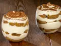 Due bicchieri di tiramisù senza uova, stratificati con crema e savoiardi, spolverati di cacao.