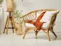 Un fauteuil en rotin tressé, invitant à la détente. Un plaid orange et un coussin blanc ajoutent une touche de confort. L'entretien rotin est essentiel pour préserver sa beauté naturelle.