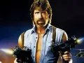 Chuck Norris z karabinami w akcji, jak w jego najlepszych filmach. W tle helikoptery i budynek.