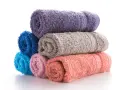 Pile de serviettes de bain roulées aux couleurs vives : violet, bleu, gris, rose et corail. La matière douce invite à la détente.