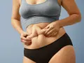 Kobieta z widocznym fałdem tłuszczu na brzuchu, mimo szczupłej sylwetki. Zjawisko "skinny fat" w praktyce.