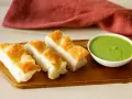 Focaccia tagliata a pezzi su tagliere di legno, accanto a una ciotola di pesto di salvia.