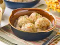 Cuatro albóndigas de merluza caseras en una cremosa salsa, espolvoreadas con perejil fresco.