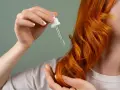 Dłoń z pipetką aplikuje olejek na rude włosy. Zastanawiasz się, ile trzymać olej na włosach?