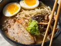 Miseczka aromatycznego ramenu z plastrami wieprzowiny, jajkiem na pół, grzybami i szczypiorkiem. Idealny ramen przepis na rozgrzewający posiłek.