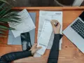 Osoba analizuje rachunki, laptop i telefon. Frankowicze nie muszą spłacać kredytu w trakcie procesu, co może być tematem analizy.