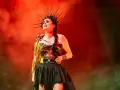 Wokalistka Within Temptation w koronie i błyszczącej kreacji, z mikrofonem w dłoni, na tle czerwonej mgły.